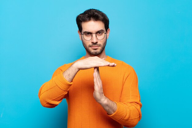 Giovane uomo bello che sembra serio, severo, arrabbiato e dispiaciuto, facendo segno di time out