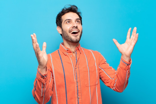 Giovane uomo bello che si sente felice, stupito, fortunato e sorpreso, celebrando la vittoria con entrambe le mani in aria