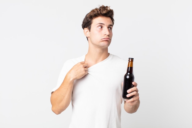 Giovane uomo bello che si sente stressato ansioso stanco e frustrato e tiene in mano una bottiglia di birra