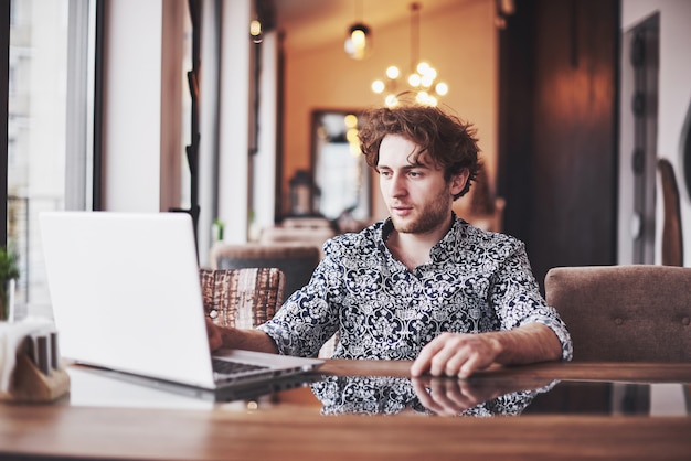 Giovane uomo bello che si siede in caffè e che lavora al computer portatile.