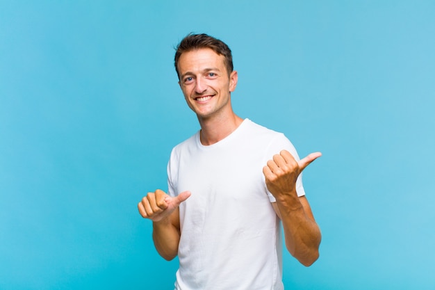 Giovane uomo bello che sorride allegramente e con indifferenza indicando lo spazio di copia sul lato, sentendosi felice e soddisfatto