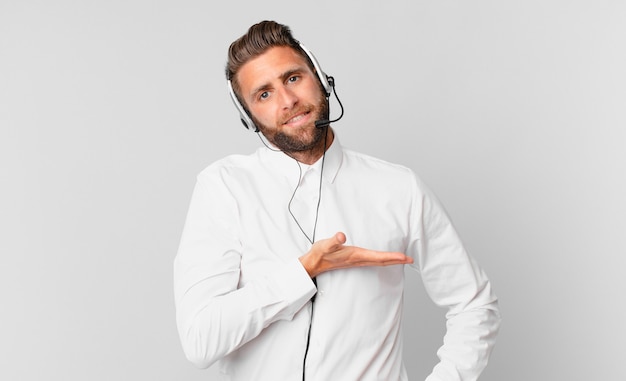 Giovane uomo bello che sorride allegramente, si sente felice e mostra un concetto. concetto di telemarketing