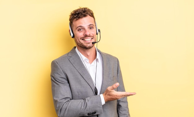 Giovane uomo bello che sorride allegramente, si sente felice e mostra un concetto. concetto di telemarketing