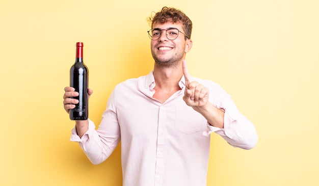 Giovane uomo bello che sorride con orgoglio e sicurezza facendo il numero uno. concetto di bottiglia di vino
