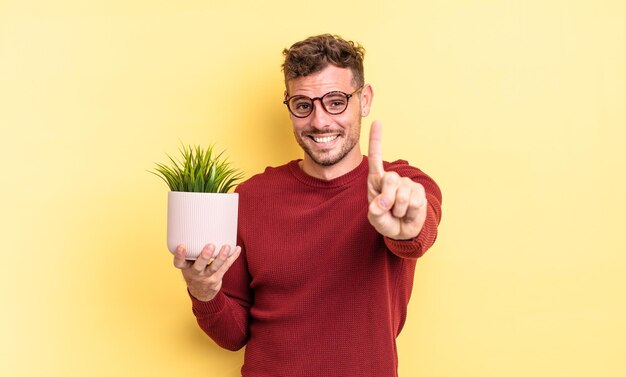 Giovane uomo bello che sorride con orgoglio e sicurezza facendo il numero uno. concetto di pianta decorativa