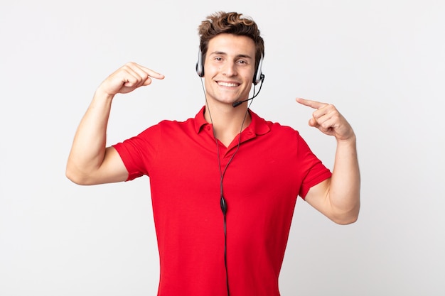 Giovane uomo bello che sorride con sicurezza indicando il proprio ampio sorriso. concetto di telemarketing