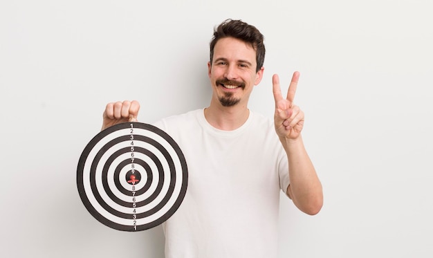 Giovane uomo bello che sorride e che sembra felice gesturing vittoria o concetto di bersaglio dardo di pace