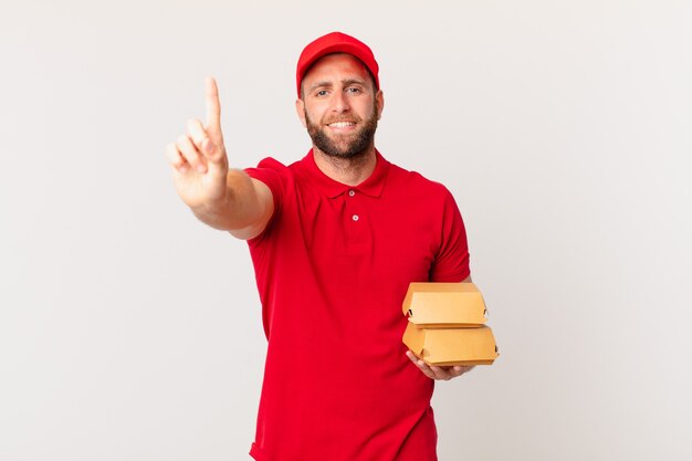 Giovane uomo bello che sorride e sembra amichevole, mostrando il concetto di consegna dell'hamburger numero uno one