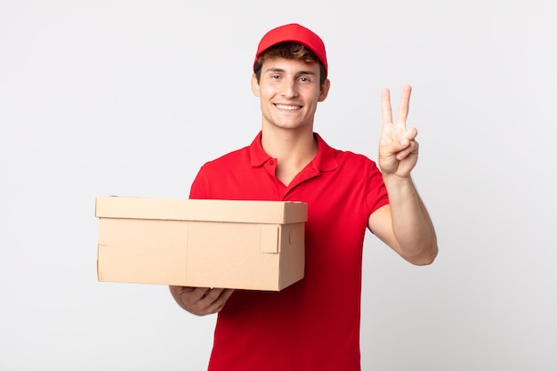 Giovane uomo bello che sorride e sembra amichevole, mostrando il concetto di servizio di pacchetto di consegna numero due.