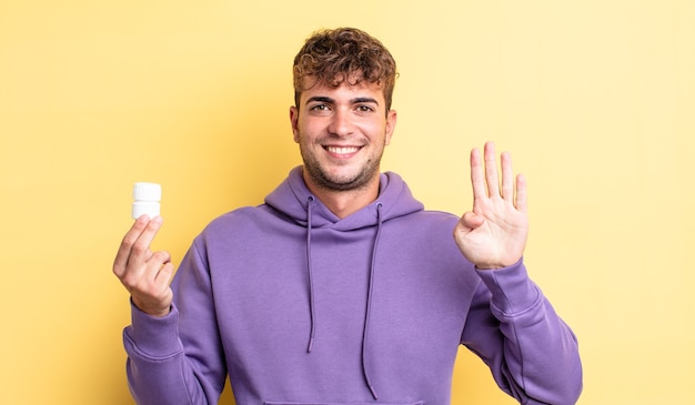 Giovane uomo bello che sorride e sembra amichevole, mostrando il numero quattro. concetto di bottiglia di pillole