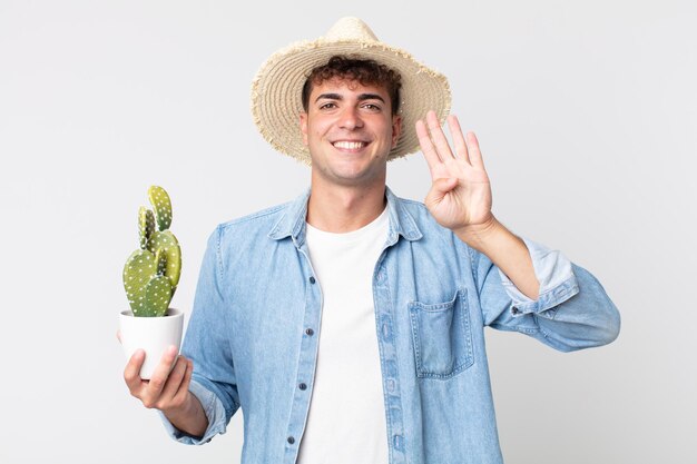 Giovane uomo bello che sorride e sembra amichevole, mostrando il numero quattro. contadino con in mano un cactus decorativo