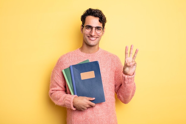 Giovane uomo bello che sorride e sembra amichevole, mostrando il numero tre. concetto di taccuino