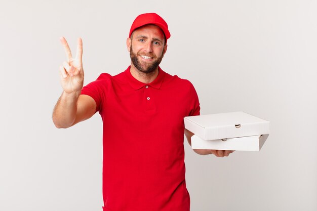 Giovane uomo bello che sorride e sembra felice, gesticolando vittoria o pace. concetto di consegna della pizza