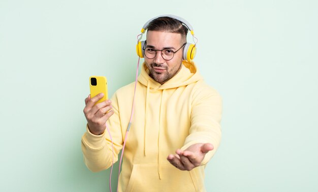 Giovane uomo bello che sorride felicemente con amichevole e offrendo e mostrando un concetto. cuffie e concetto di smartphone