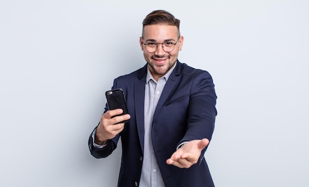 Giovane uomo bello che sorride felicemente con amichevole e offrendo e mostrando un concetto di business e smartphone