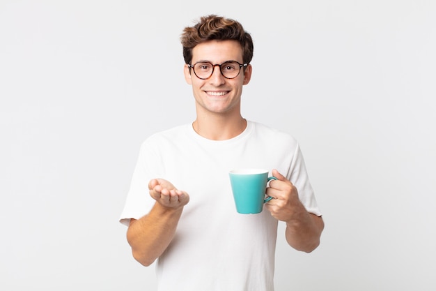 Giovane uomo bello che sorride felicemente con amichevole e offrendo e mostrando un concetto e tenendo in mano una tazza di caffè