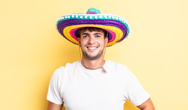 Giovane uomo bello che sorride felicemente con una mano sull'anca e fiducioso. concetto di cappello messicano