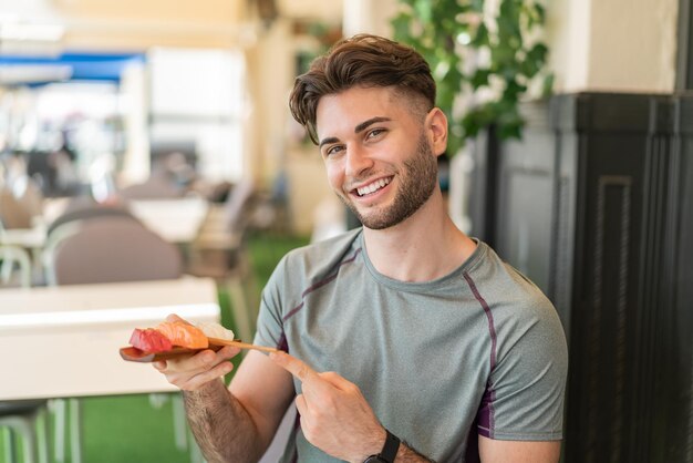 Giovane uomo bello che tiene il sashimi all'aperto e lo indica