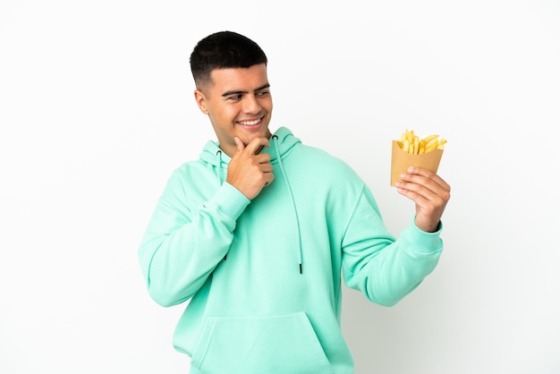 Giovane uomo bello che tiene patatine fritte su sfondo bianco isolato guardando di lato e sorridente