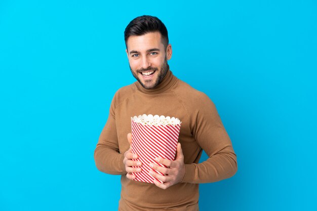 Giovane uomo bello che tiene un grande secchio di popcorn