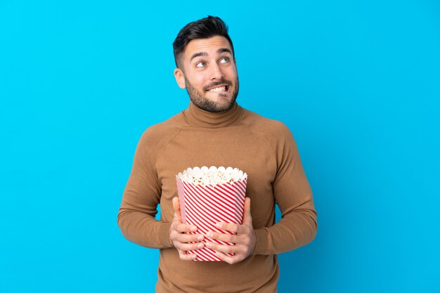 Giovane uomo bello che tiene un grande secchio di popcorn