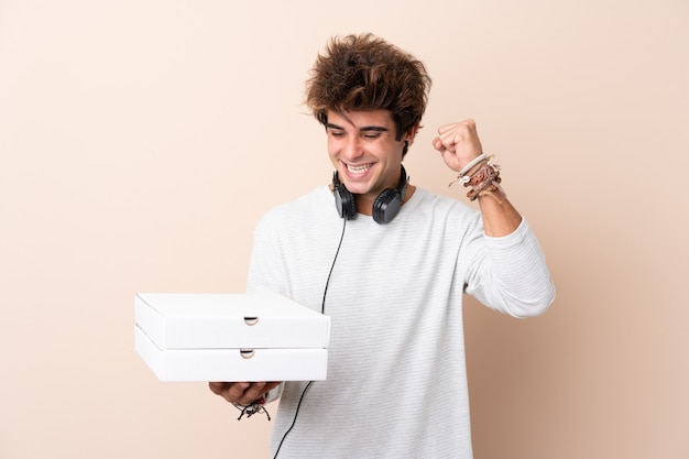 Giovane uomo bello che tiene una pizza sopra la parete isolata che celebra una vittoria