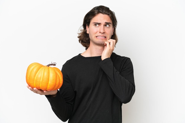 Giovane uomo bello che tiene una zucca isolata su sfondo bianco con dubbi e pensare