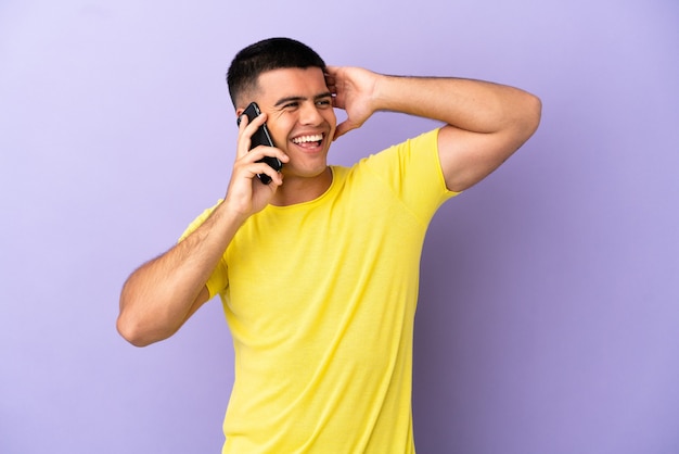 Giovane uomo bello che usa il telefono cellulare sul muro viola isolato che sorride molto