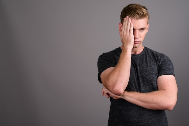 Giovane uomo bello con capelli biondi che indossa camicia grigia sulla parete grigia