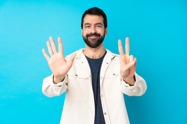 Giovane uomo bello con giacca di velluto bianco su muro blu isolato contando sette con le dita