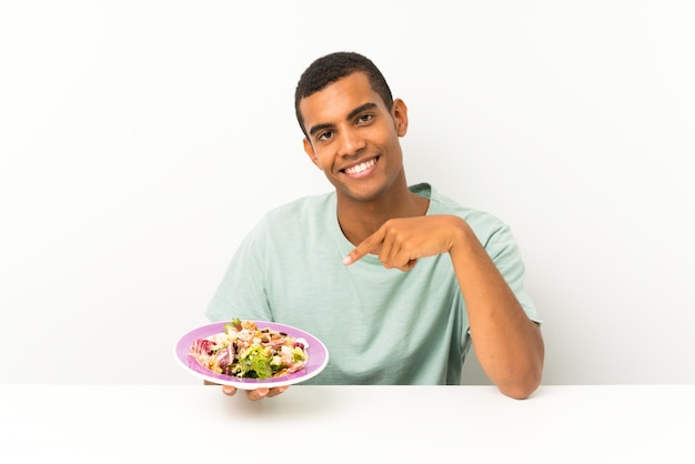 Giovane uomo bello con insalata in una tabella