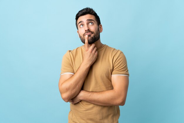 Giovane uomo bello con la barba che ha dubbi mentre guarda in alto