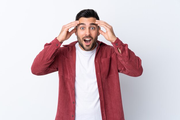 Giovane uomo bello con la barba che indossa una giacca di velluto a coste su sfondo bianco isolato con espressione di sorpresa