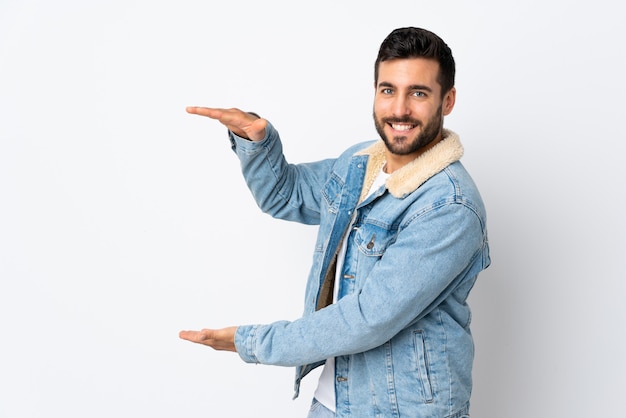 Giovane uomo bello con la barba isolata sul copyspace bianco della tenuta della parete per inserire un annuncio