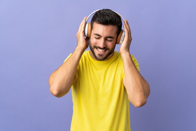 Giovane uomo bello con la barba isolata sulla musica d'ascolto viola