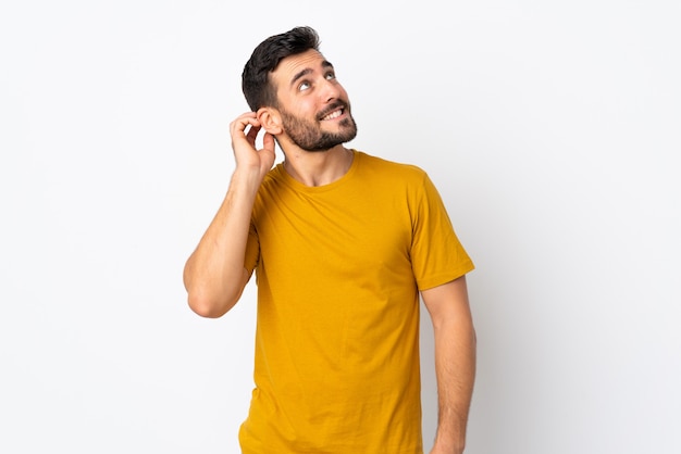 Giovane uomo bello con la barba isolata sulla parete bianca che pensa un'idea