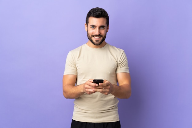 Giovane uomo bello con la barba sopra isolato inviando un messaggio con il cellulare