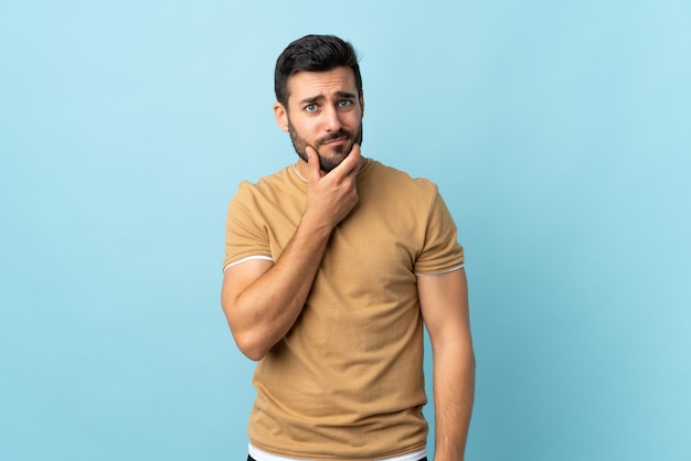 Giovane uomo bello con la barba sopra la parete isolata che ha dubbi