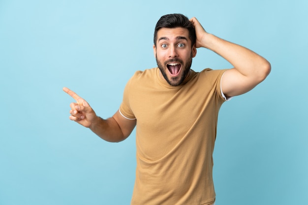 Giovane uomo bello con la barba sorpreso e puntando il dito verso il lato