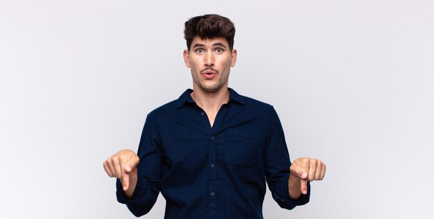 Giovane uomo bello con la bocca aperta rivolta verso il basso con entrambe le mani, guardando scioccato, stupito e sorpreso