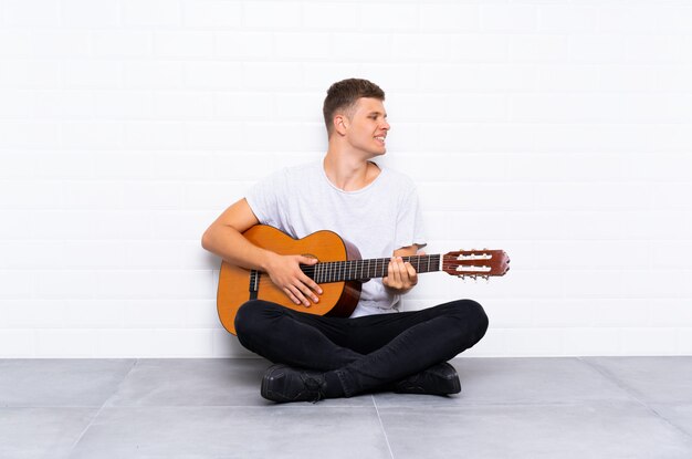 Giovane uomo bello con la chitarra che sembra laterale