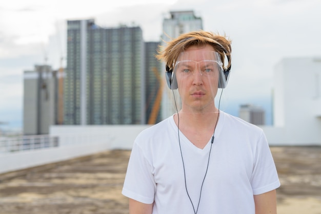 Giovane uomo bello con la visiera che ascolta la musica sul tetto dell'edificio