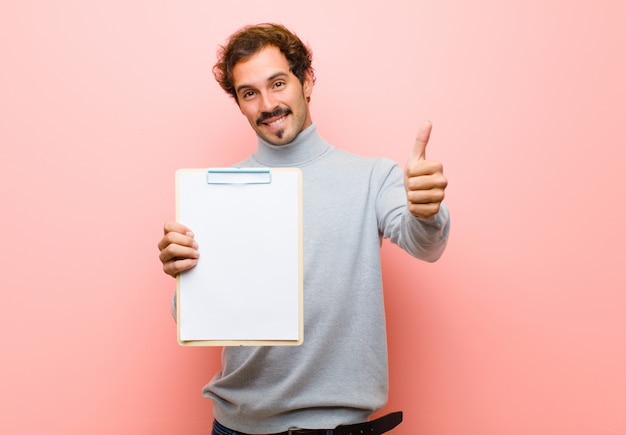 Giovane uomo bello con un foglio di carta contro la parete piana rosa