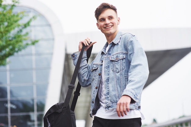 Giovane uomo bello con una borsa sulla spalla in fretta per l'aeroporto.