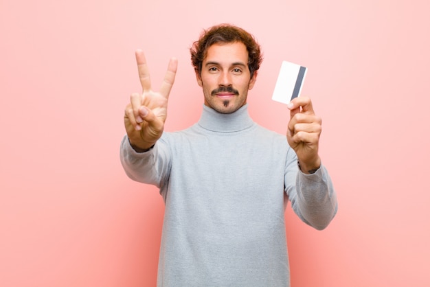 Giovane uomo bello con una carta di credito contro la parete piana rosa