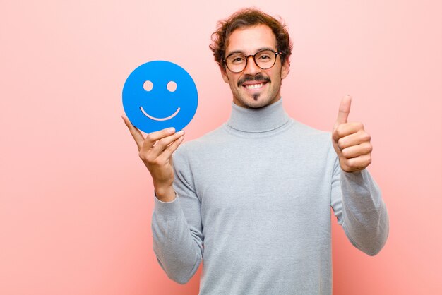 Giovane uomo bello con una faccia sorridente contro il piano rosa