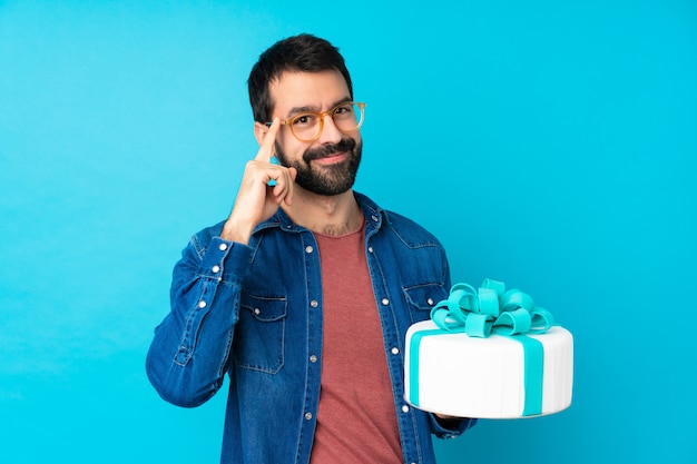 Giovane uomo bello con una grande torta sul blu con gli occhiali e felice