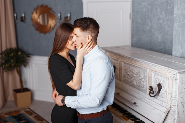 Giovane uomo bello con una ragazza felice in abiti eleganti che abbraccia vicino a un pianoforte d'epoca