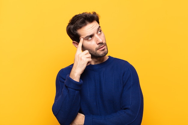 Giovane uomo bello con uno sguardo concentrato, chiedendosi con un'espressione dubbiosa, guardando in alto e di lato