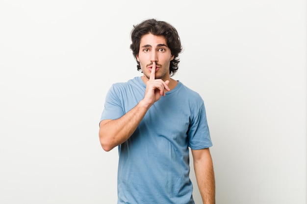 Giovane uomo bello contro un muro bianco mantenendo un segreto o chiedendo silenzio.